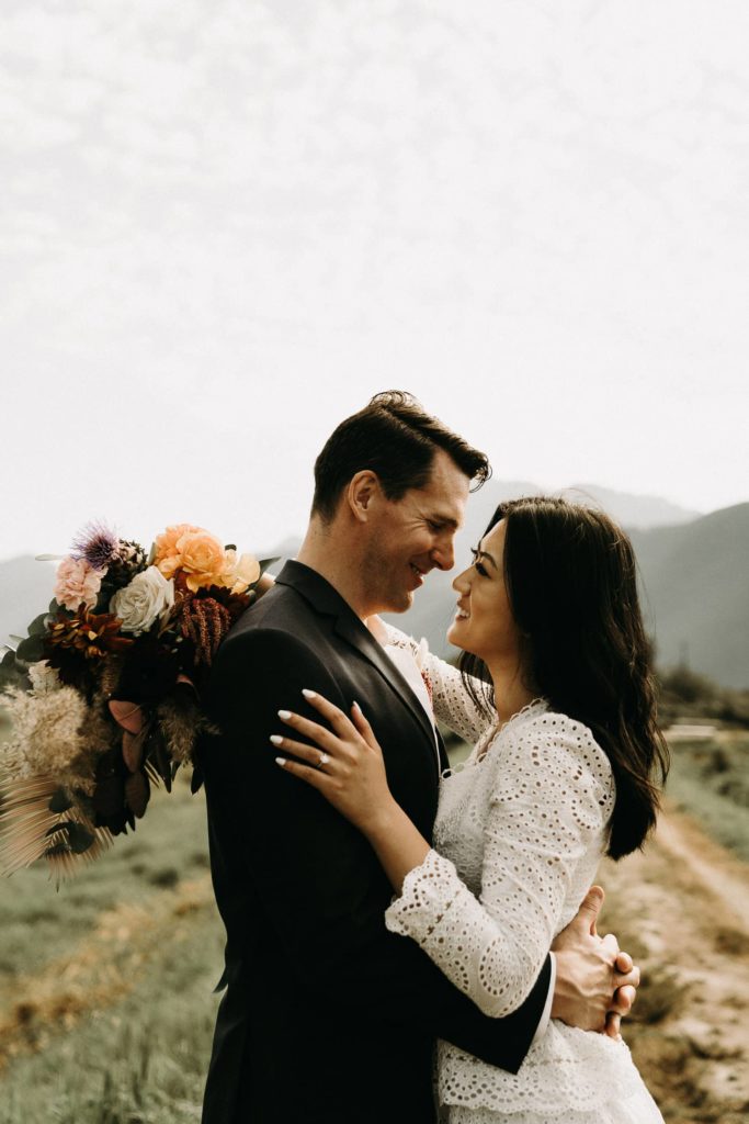 bride and groom smiling hugging with wedding bouquet at pitt lake
