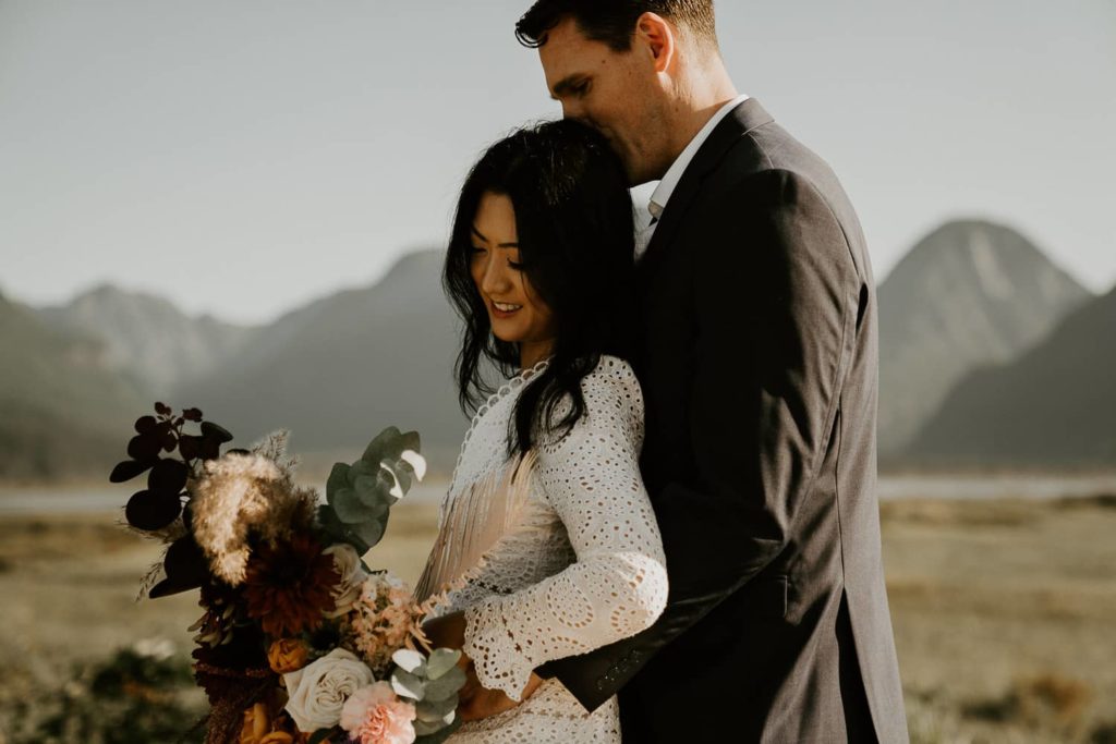 groom kissing bride head with the wedding bouquet at pitt lake