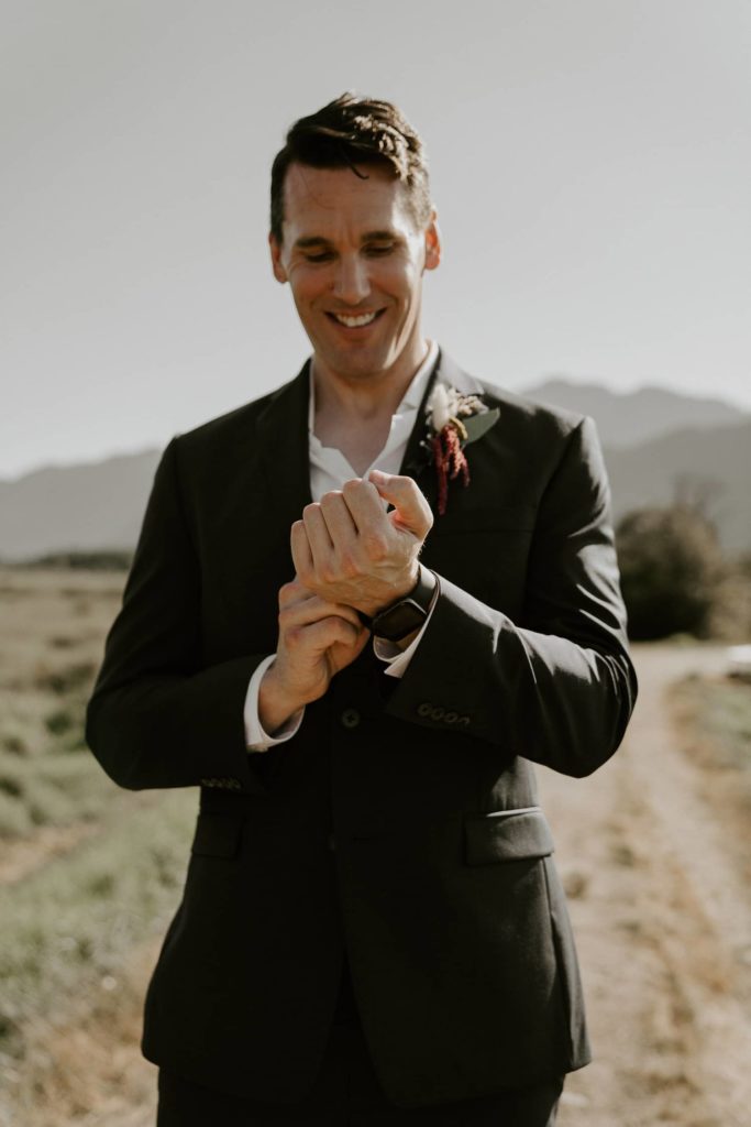 groom smiling with his boutonniere and adjusting his watch at pitt lake