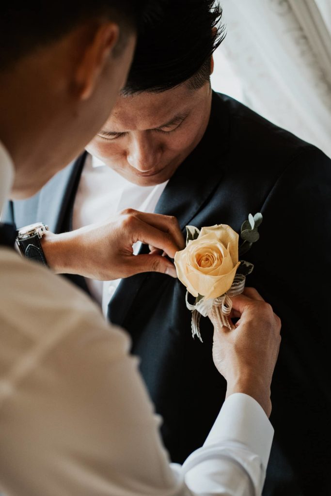 Groomsmen adjusting groom boutonniere with orange rose